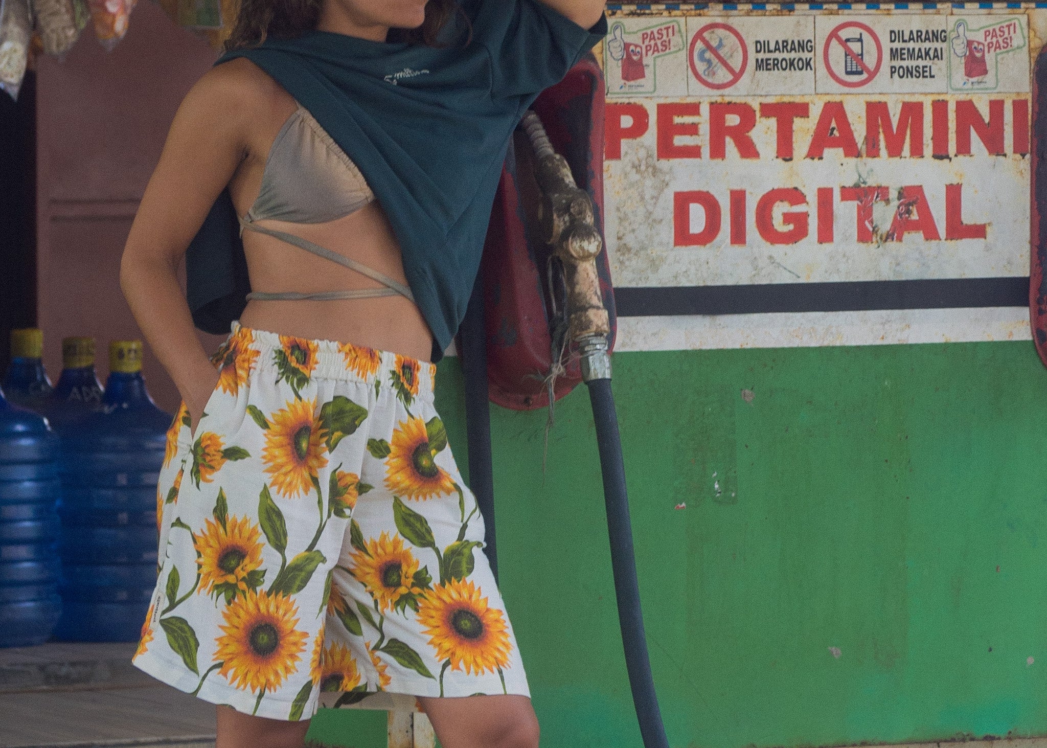 Person wearing a floral skirt and sleeveless top in front of a Pertamin Digital sign.